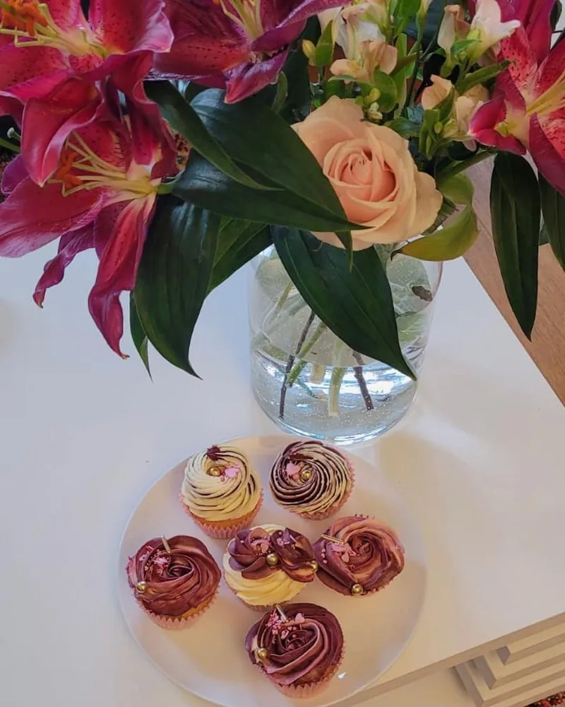 Burgundy and cream rose cupcakes with gold pearls beside pink lilies
