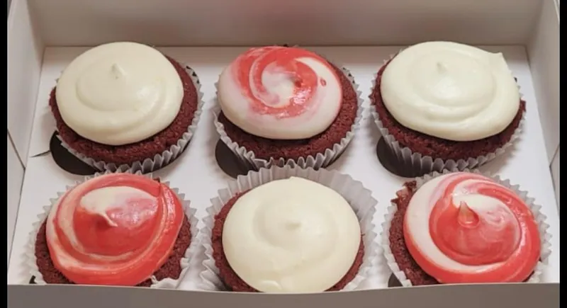 Six red velvet cupcakes with white and red swirled cream cheese frosting