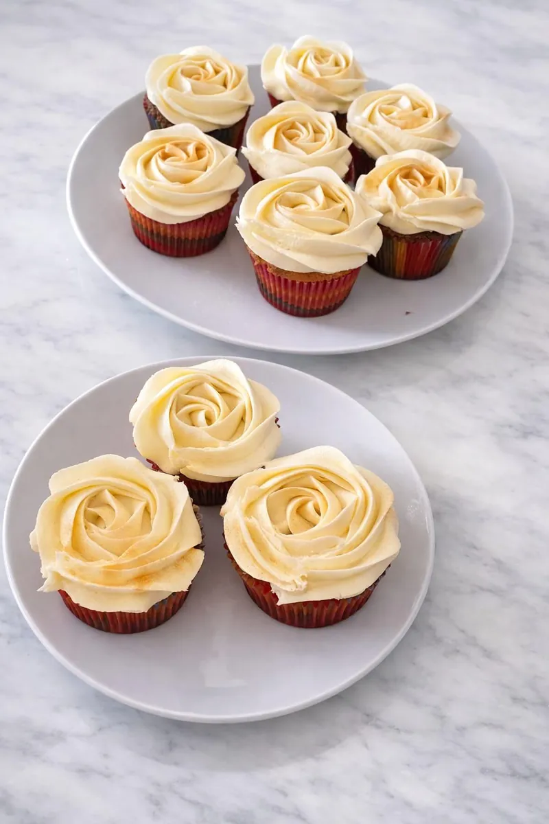 Ivory rose-piped cupcakes with a light gold dusting on two plates